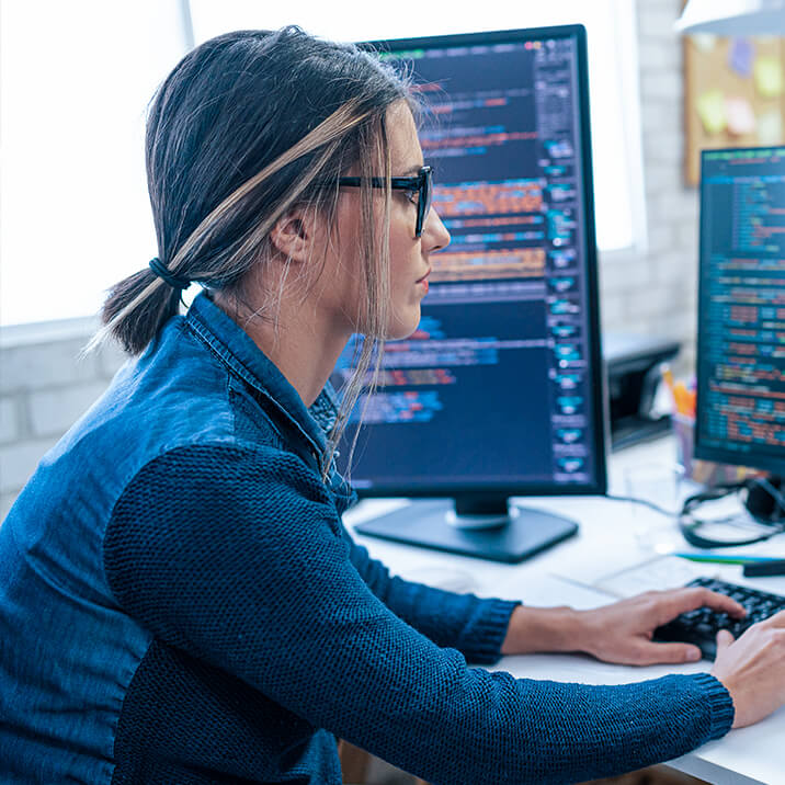 A female programmer uses two monitors to work on code for a custom software development project.